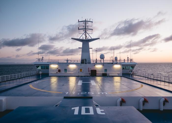 A pink sky at dusk sets on the bow of a Marine Atlantic ferry as it sails in the ocean, illuminating the boat's helipad.