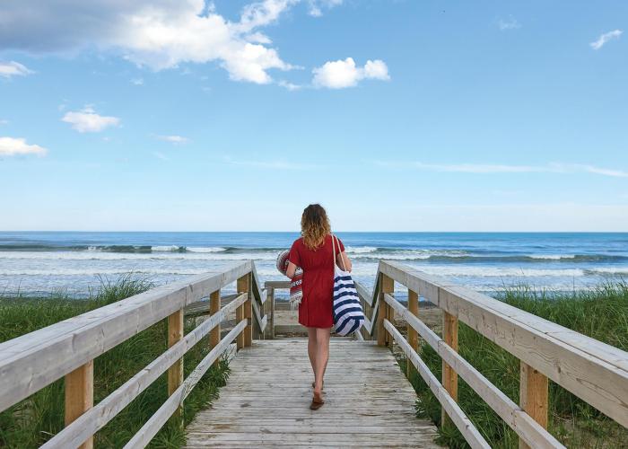 Woman waling onto beach from boardwalk.