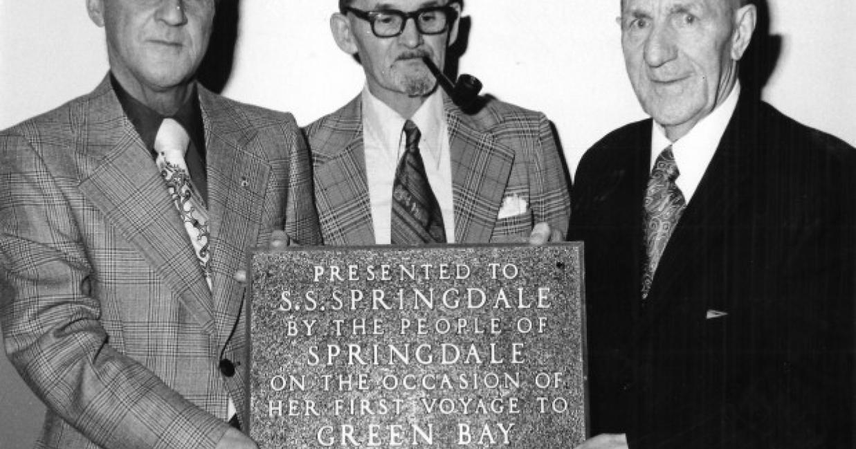 three men holding a plaque