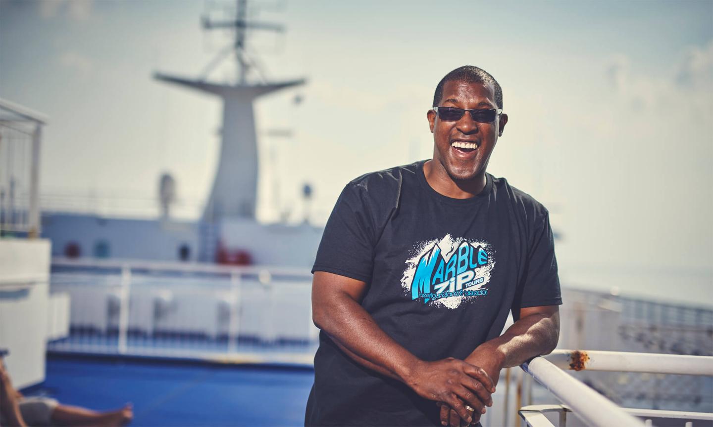 A smiling man in sunglasses leaning against the railing of a ferry deck.