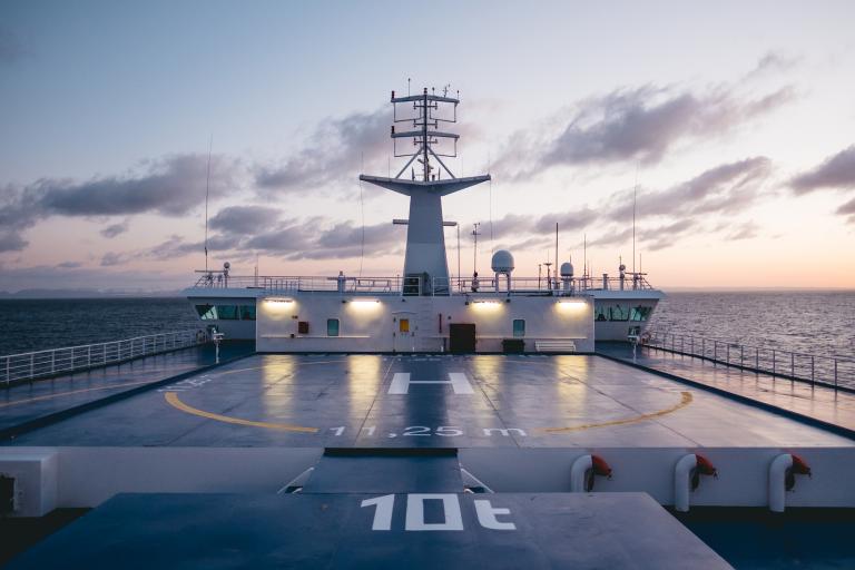 A pink sky at dusk sets on the bow of a Marine Atlantic ferry as it sails in the ocean, illuminating the boat's helipad.