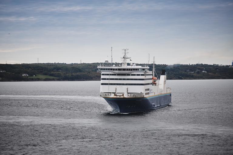 The Marine Atlantic MV HIghlanders ferry is flanked by green tree-covered shores as it sails out of port on an overcast day.