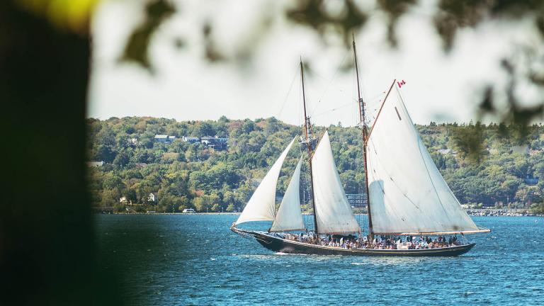 The tourist filled Bluenose II, a replica of the famous racing schooner, sails past the tree-lined hills of Lunenburg Harbour.