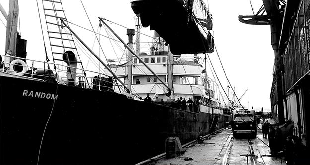 Image: black and white, bus being loaded by crane onto the SS Random