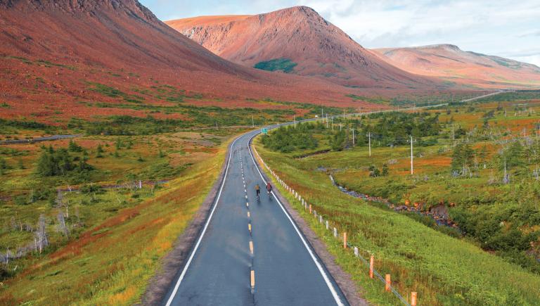 two bikers on empty road with mountains in background