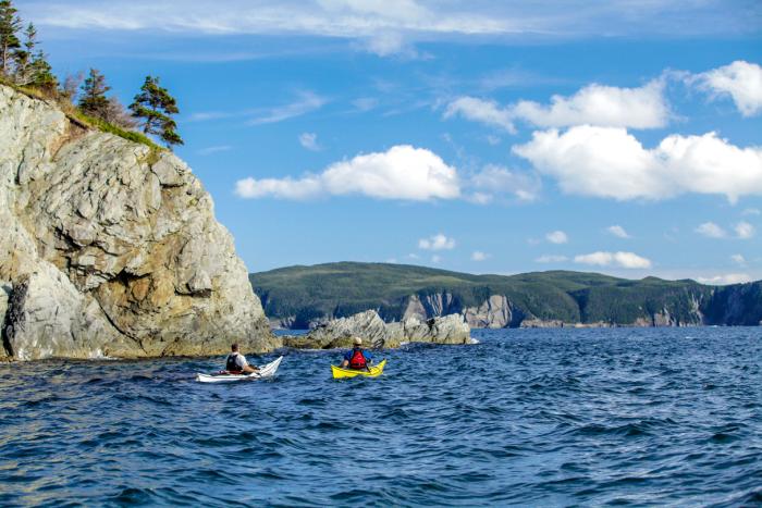 two kayakers on water alongside steep rocky cliff