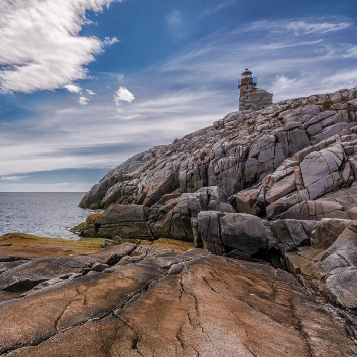 the Rose Blanche lighthouse sits on rocky water's edge with cloudy sky in background