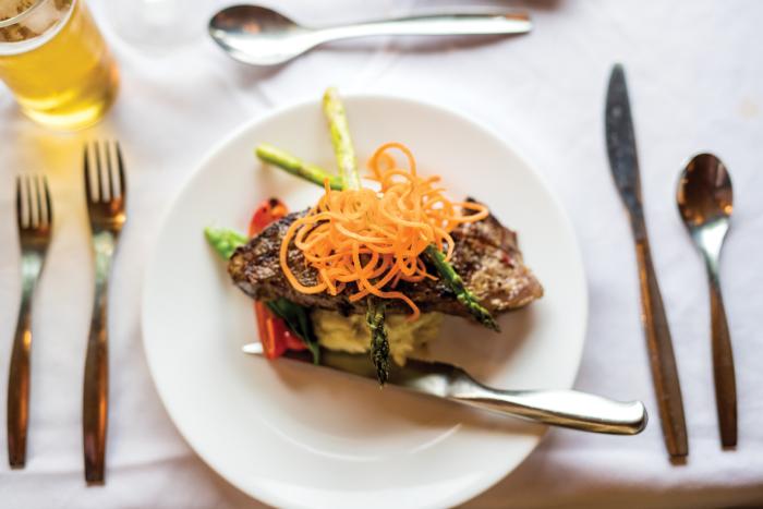 a white plate of seared meat covered in asparagus and spiralized carrots sits on table with cutlery