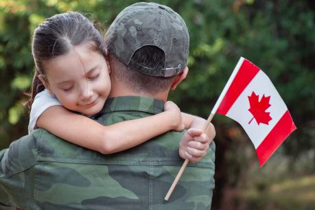 a child hugs a person in a uniform while holding Canada flag