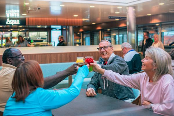 Group of four people holding their drinkware in the middle of the table saying cheers