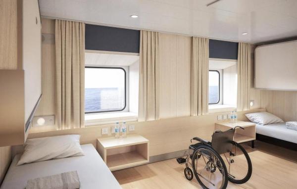 Accessible cabin with two single beds, wide open floor space, and a wheelchair positioned between windows overlooking the ocean