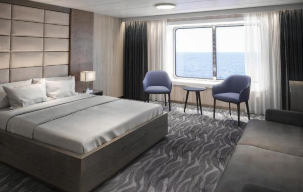 Deluxe cabin with a queen bed, upholstered headboard, two lounge chairs by a large window, and a sofa with ocean views