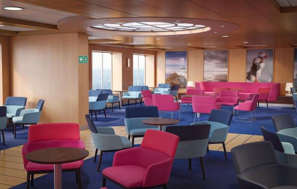Lounge area with armchairs and sofas, round wood tables, and wall art of coastal scenes and a puffin